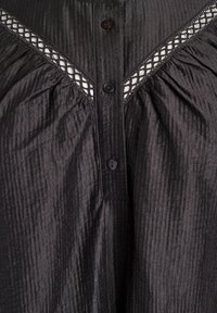 Čierna blúzka s textúrou a gombíkmi na prednej strane, s krajkovým pásom s diamantom pozdĺž ramien.