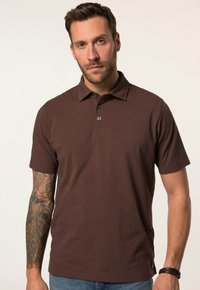 Hnědá polo tričko vyrobené z měkké tkaniny, s límcem, zapínáním na tři knoflíky a krátkými rukávy. Obsahuje jemné brandování na lemu.