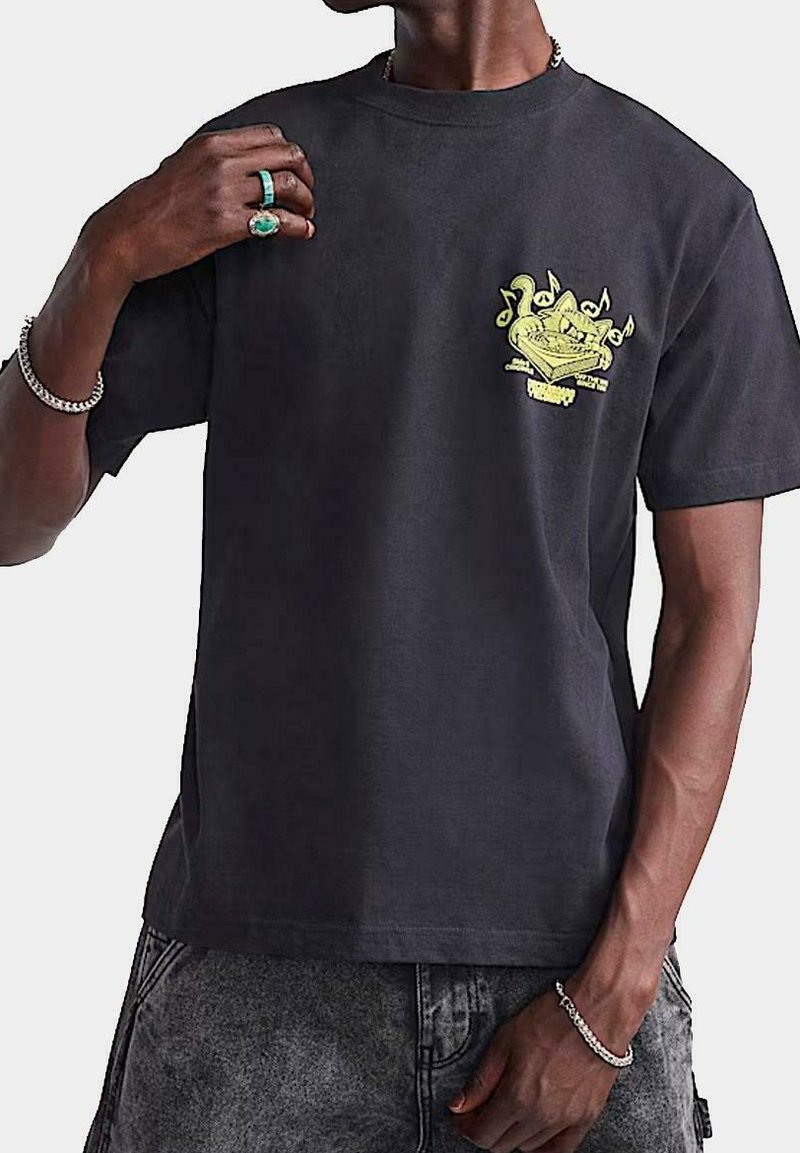 Camiseta de algodón negra con un diseño gráfico amarillo brillante en el lado izquierdo del pecho. Manga corta, cuello redondo y corte relajado.