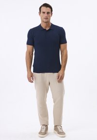 Mørkeblå polo med kortærmer i kabelstrik, parret med beige tapered bukser og lysebrune sneakers. Minimalistisk design.