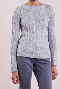 Vaaleanharmaa neulottu villapaita, jossa on ribbireunus, pitkät hihat ja leveä pyöreä kaula-aukko, käytetty harmaiden housujen päällä.