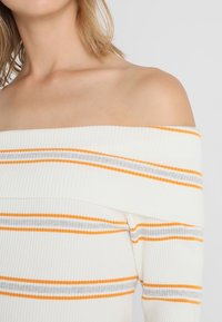 Off-the-shoulder ribbed top in white, featuring orange and grey horizontal stripes, with a soft texture and fitted design.