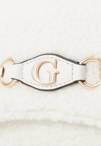 Bijela pahuljasta tkanina s zlatnim akcentom logotipa "G" i kožnim remenom. Sadrži okruglu metalnu opremu i kontrastne tamne šavove.