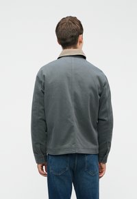 Grijze fleecejas met een beige kraag, met een relaxte pasvorm en lange mouwen, gecombineerd met blauwe denim jeans.