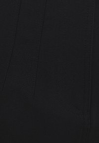 Närbild av svart tyg med synliga vertikala och böjda sömdetaljer.