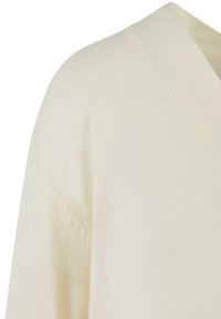 Pull à col V de couleur crème, avec une texture douce et des détails de couture visibles. Le tissu est léger et légèrement élastique.