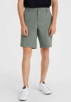 Pantalones cortos verde claro de algodón, con un diseño plano al frente, cierre de botón y bolsillos laterales. Combinados con zapatillas blancas.