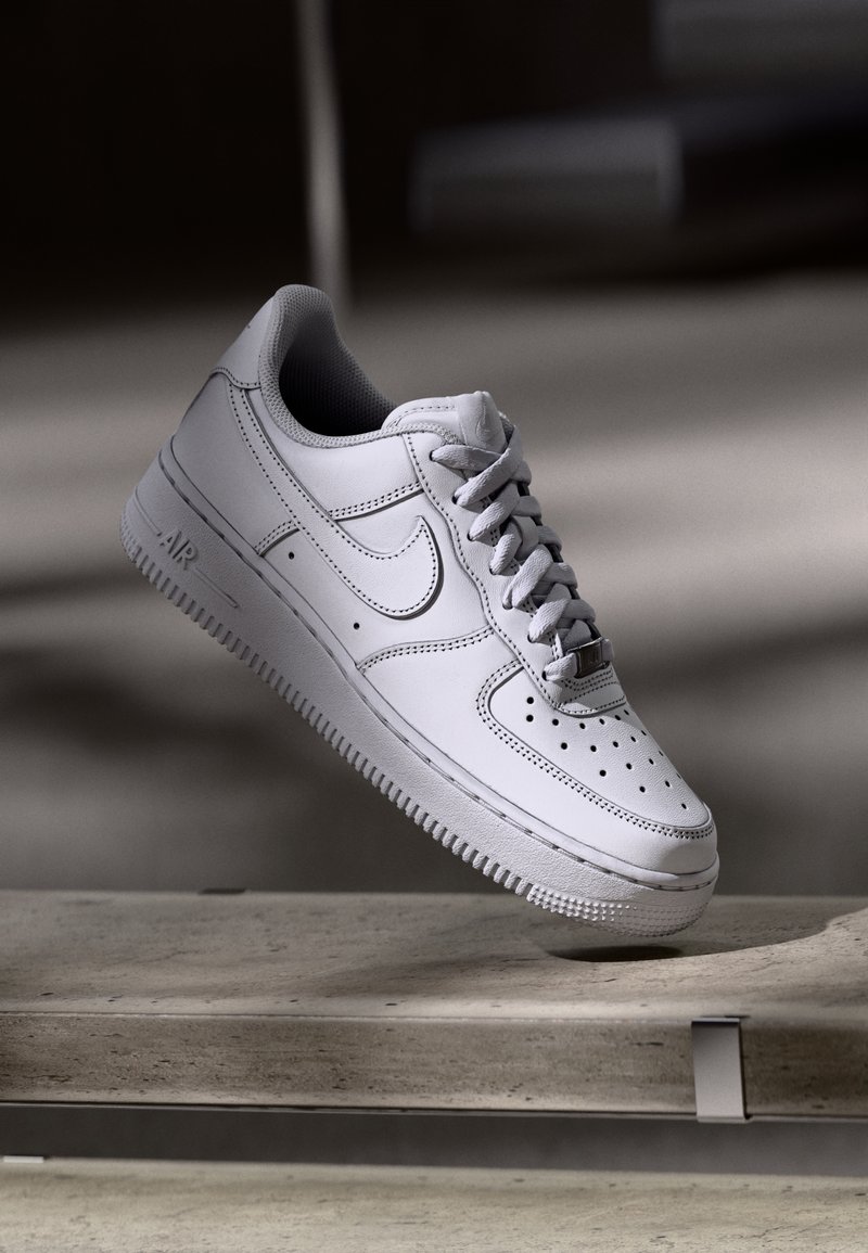 White leather Nike Air Force 1 sneaker features a perforated toe, flat laces, and textured rubber sole with “AIR” branding on the side.