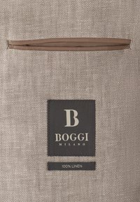 Tissu en chevrons beige avec une poche intérieure marron et deux étiquettes : une noire "Boggi Milano" et une plus petite indiquant "100 % lin".