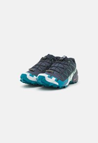 Baskets de sport bleu foncé avec des accents verts, tige en maille texturée et semelle à motif turquoise et blanc. Équipées d'un système de laçage rapide.