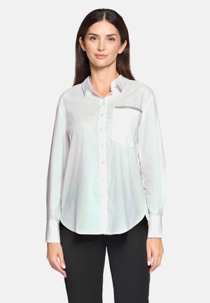 White button-up shirt in lightweight fabric with a chest pocket featuring a black trim accent. Long sleeves, curved hem, and smooth texture.