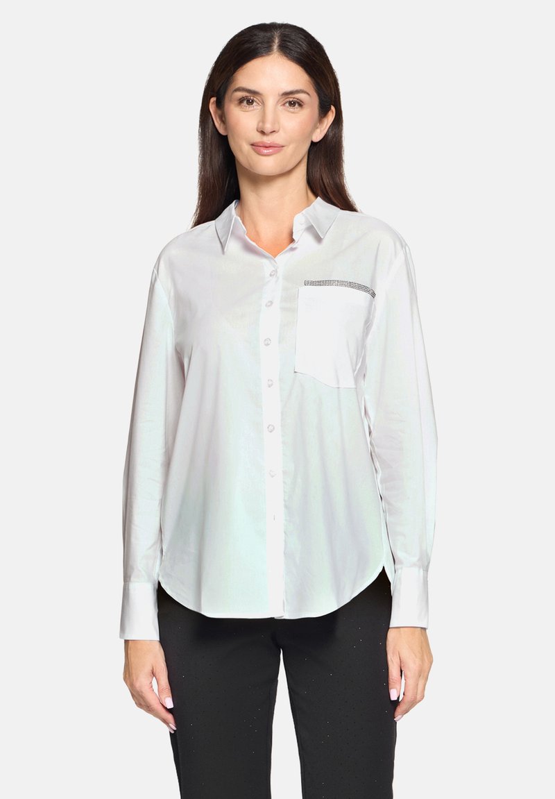 White button-up shirt in lightweight fabric with a chest pocket featuring a black trim accent. Long sleeves, curved hem, and smooth texture.