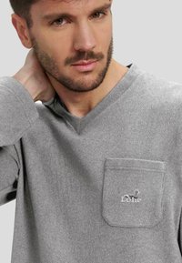 CamIsa gris de manga larga con escote en V y un bolsillo delantero que presenta un pequeño logotipo bordado. La textura parece suave y la tela es lisa.