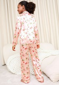 Rosa satinpyjamas med ett festligt tryck med julmotiv, långa ärmar och matchande byxor, accentuerade med en dekorativ trim.