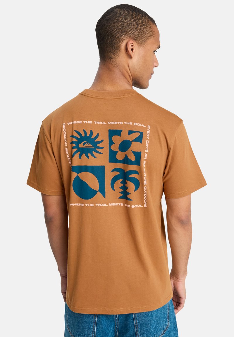 Homme portant un T-shirt marron avec des graphismes bleus de soleil, fleur, cercle et palmier, et un texte blanc autour des motifs au dos.