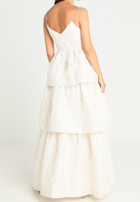 Valkoinen, kerroksellinen mekko, jossa on teksturoitu kangas, ohut olkaimet ja V-mallinen selkäosa. Kolme erilaista kerrosta luo volyymiä.