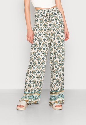 Pantalons évasés en tissu blanc avec un motif coloré de paisley et de fleurs. Les pantalons ont une taille à nouer et un ourlet à motif contrasté.
