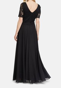 Zwart avondjurk met een kant bodice, korte mouwen en een vloeiende, geplooide rok. Heeft een V-achter ontwerp en een verborgen rits sluiting.