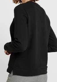 Sudadera negra con cuello redondo, puños acanalados y dobladillo recto. Tela suave con una textura lisa, que presenta un detalle mínimo.
