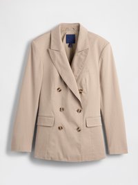 Blazer beige à double boutonnage avec deux poches avant, revers crantés et boutons ronds. Fabriqué en tissu lisse avec une texture minimale.