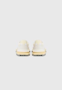 Sneakers met een witte bovenkant met gele accenten, een gestructureerde grijze zool en een geveerd hiel. Het ontwerp bevat driehoekige details aan de achterkant.