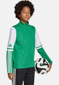 Groene sweatshirt met witte mouwen en drie-strepenaccenten; gladde textuur; staat met een voetbal in de hand.