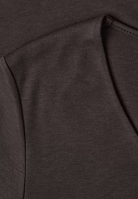 Gros plan d’un tissu marron foncé montrant des coutures piquées et des bords pliés d’un vêtement en maille doux.