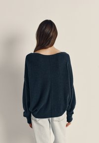 Overdimensioneret, mørkegrå sweater med bred udskæring, sænkede skuldre og struktureret stof. Samlet med lyse, løst siddende jeans.