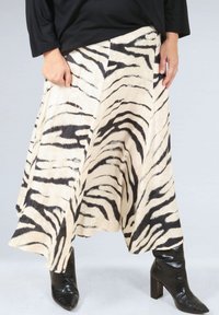 Zebra-patterned skirt in cream and black, made from a lightweight fabric, features an A-line shape and drapes to mid-calf. Paired with black boots.