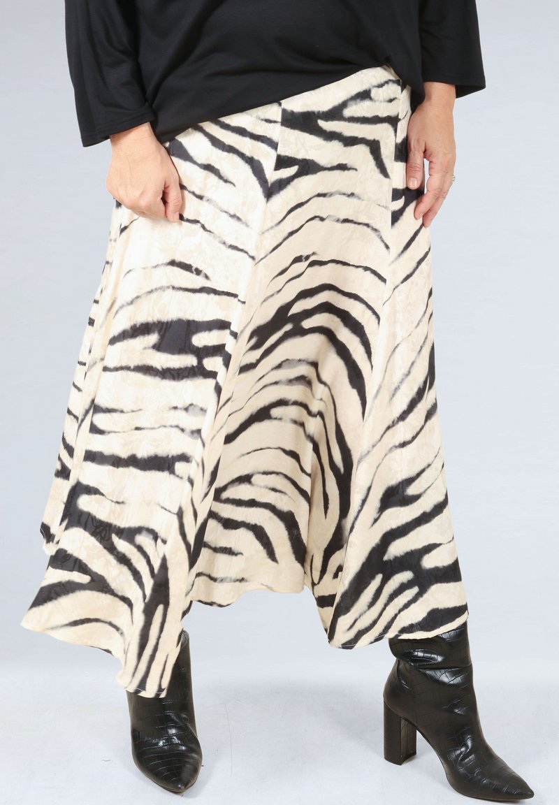 Zebra-patterned skirt in cream and black, made from a lightweight fabric, features an A-line shape and drapes to mid-calf. Paired with black boots.