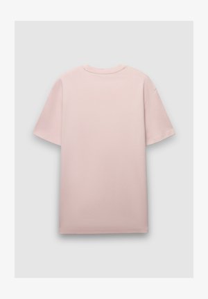 Maglietta oversize rosa con maniche corte, scollo rotondo e texture liscia. Il tessuto appare morbido e leggero, senza motivi visibili.