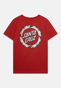Sarkans kokvilnas T-krekls ar apaļu grafiku, kurā ir teksts "SANTA CRUZ" treknā baltā fontā, ko ieskauj melnas un baltas liesmas.