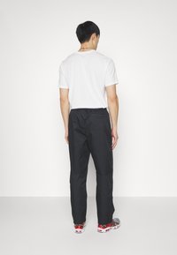 Svarta lätta byxor med elastisk midja, slät yta och lös passform, kombinerade med flerfärgade sneakers och en vit t-shirt.