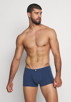 Heren blauwe katoen boxershorts met een aansluitend ontwerp, gladde textuur en een zwart logo op de tailleband; model geposeerd tegen een neutrale achtergrond.