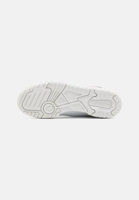 Bílá sportovní podešev s texturovanou gumou, která obsahuje drážky, výstupky a značení "New Balance". Čistý, minimalistický design.