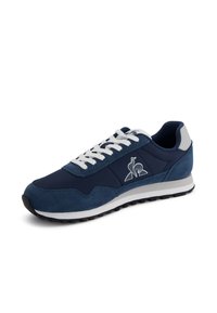 Navy blue sneakers with suede and mesh materials, white laces, and logo detail on the side. Features a contrasting white midsole and rubber outsole.