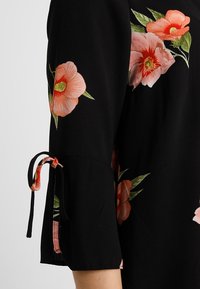 Black fabric sleeve with large pink and orange floral prints and a tied bow detail near the elbow.
