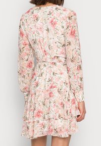 Robe fleurie à manches longues, tissu rose pastel, ourlet volanté et taille ceinturée, avec un mélange de motifs floraux rose et vert.