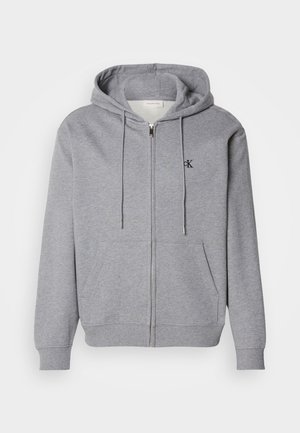 Gray zip-up hoodie made of soft fabric, featuring a hood, drawstrings, two front pockets, and a small black logo on the chest.