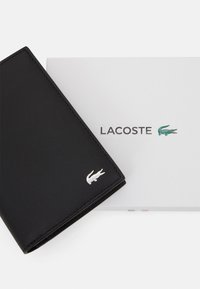Schwarzes Lederportemonnaie mit silbernem Lacoste-Logo. Verfügt über ein elegantes Design, eine glatte Textur und wird in einer weißen Markenbox geliefert.
