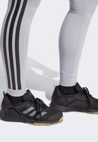 Los zapatos deportivos negros cuentan con una parte superior de malla, acentos grises y suela de goma. Se llevan con leggings blancos ajustados con rayas verticales negras.