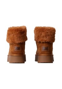 Bottines en daim marron avec un revers en fourrure douce, dotées d'une semelle en caoutchouc et de détails cousus, marquées d'une étiquette beige sur le talon.