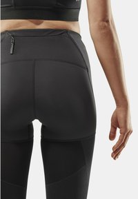 High-waisted black leggings with textured fabric, featuring a small zip pocket on the back and seam detailing along the hips and thighs.