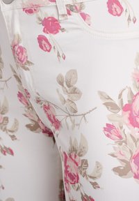 Jeans blancos con un patrón floral en rosa y beige; cuentan con una textura suave, diseño de cinco bolsillos y herrajes de botón plateados.