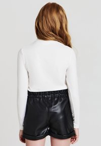Maglietta bianca a maniche lunghe abbinata a pantaloni corti neri in pelle sintetica a vita alta. I pantaloni corti hanno una cintura elastica e un orlo arrotolato.