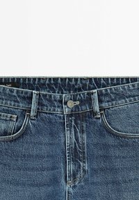Denim jeans with a dark blue color, faded texture, classic five-pocket design, metal button closure, and a stitched waistband.