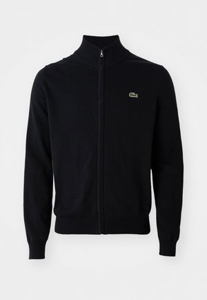 Black zip-up cardigan with ribbed collar, cuffs, and hem, featuring a small green crocodile logo on the left chest.