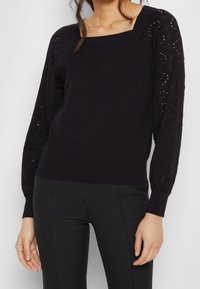 Svart stickad tröja med fyrkantig halsringning, som har texturerade, öppen arbetsärmar och en figurnära nederdel. Lämplig för lager-på-lager-styling.