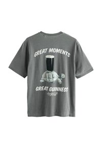 Graues Baumwoll-T-Shirt mit einer Schildkrötenillustration, die ein Pint Stout auf dem Rücken trägt, der Text lautet: "Großartige Momente, großartiges Guinness."