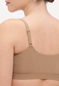 Smeđi bešavni grudnjak s podesivim trakama, glatkom teksturom i bez vidljivih šavova ili metalnih dijelova. Minimalistički dizajn pogodan za razne bluze.